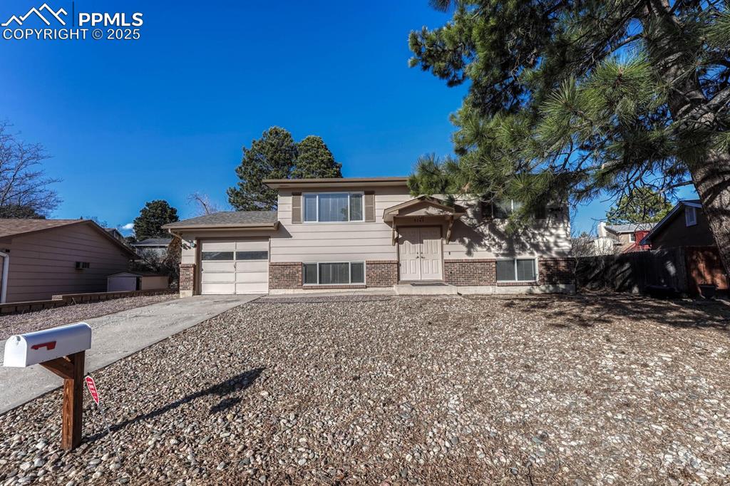 Image 2 of 43: Bi-level home with brick siding, driveway, and an attached garage