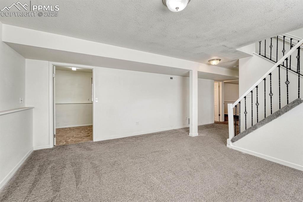 Image 25 of 43: Finished basement with a textured ceiling, carpet flooring, and stairs