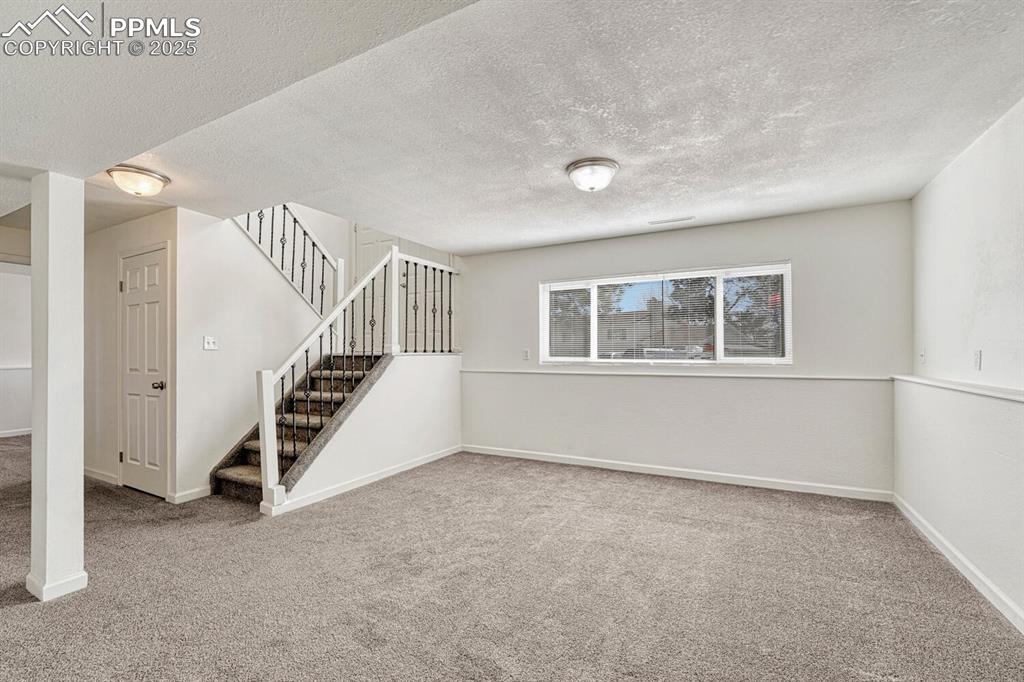 Image 26 of 43: Below grade area featuring a textured ceiling, carpet flooring, and stairwa