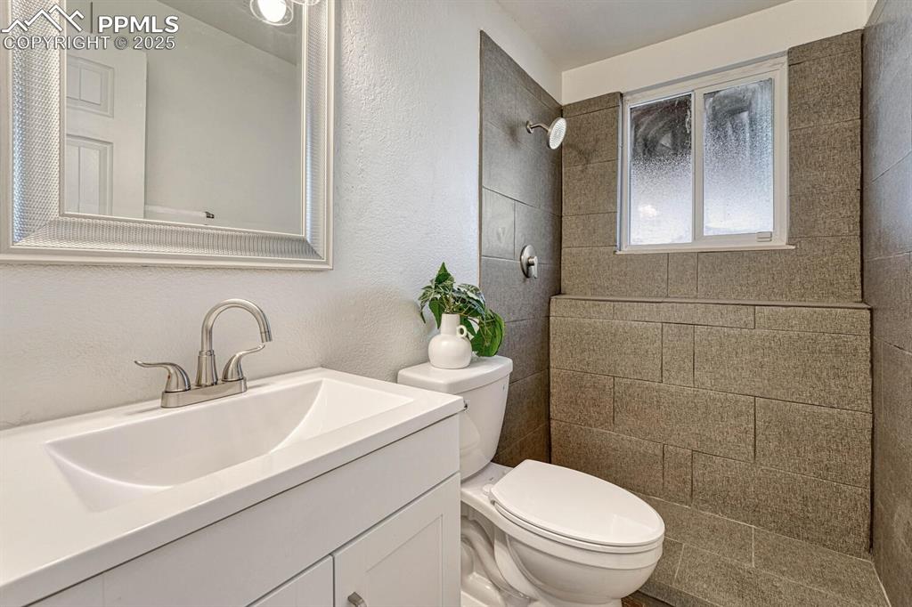 Image 27 of 43: Bathroom featuring a textured wall, a tile shower, and vanity
