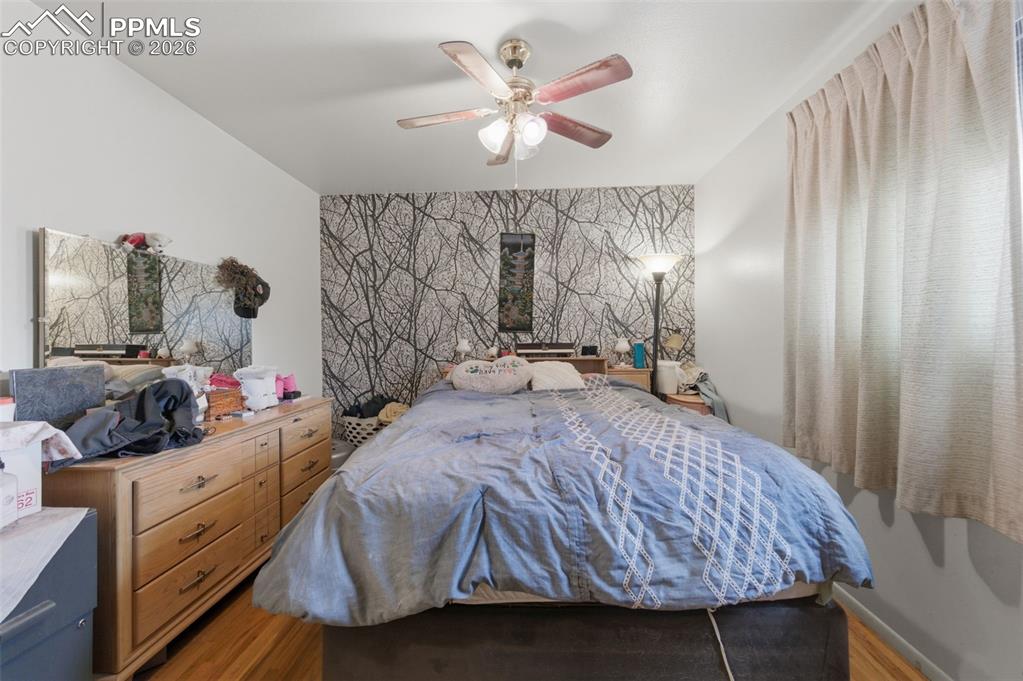 Image 14 of 24: Bedroom featuring a decorative accent wall, wood-finish flooring, and a cei