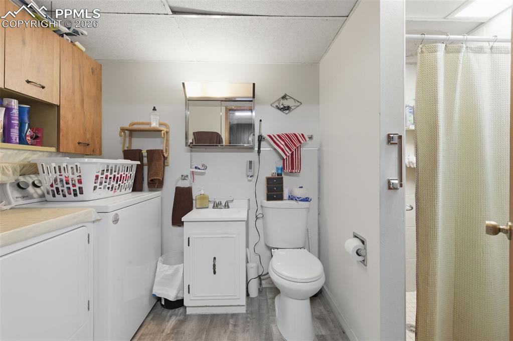Image 19 of 24: Compact utility room featuring wood-finish flooring, a white vanity with an
