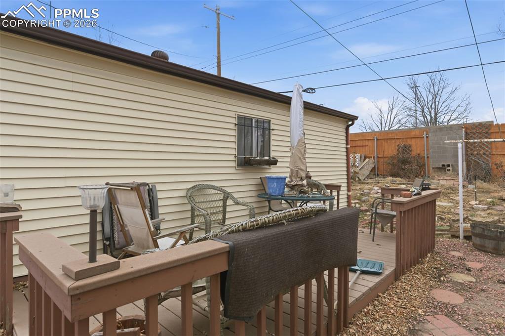 Image 22 of 24: Rear deck with wood railing, tan siding, and a window with a security grill