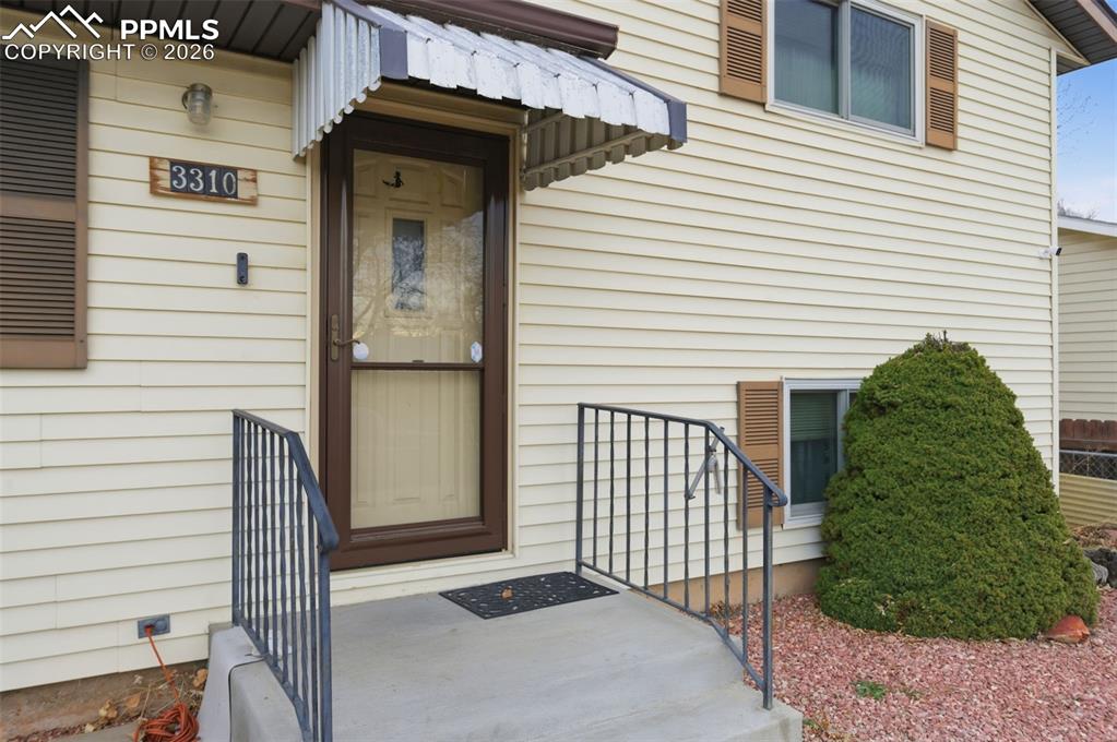 Image 4 of 24: Front entry featuring a storm door, corrugated awning, and house number