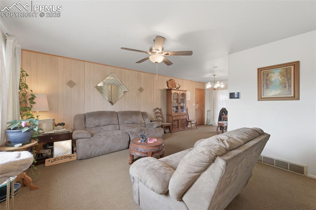Image 5 of 24: Living area featuring carpeting, wood-paneled accent wall, ceiling fan with