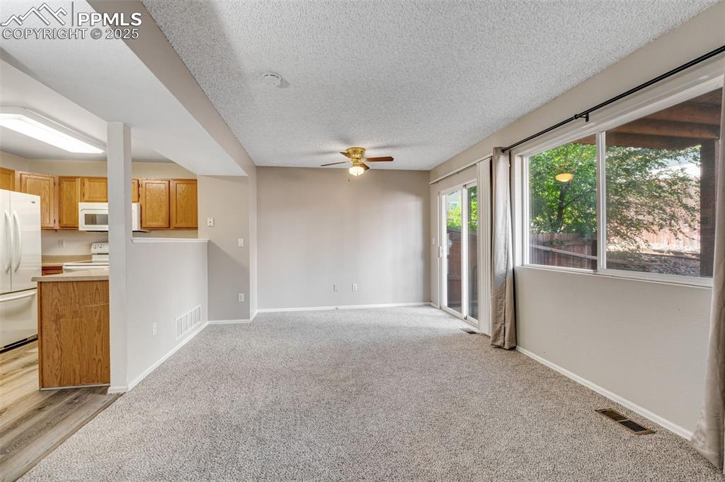 Image 6 of 30: Unfurnished living room featuring a ceiling fan, light carpet, and a textur