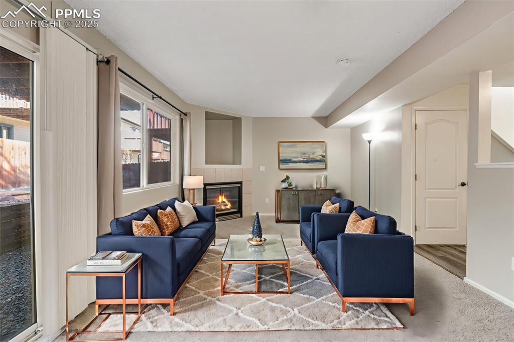 Image 9 of 30: Virtual Stage. Carpeted living room featuring a tiled fireplace and baseboa