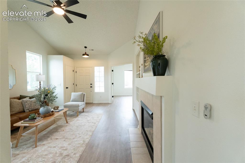 Image 6 of 26: Vaulted ceiling with a ceiling fan, fireplace with a mantel, wood-finish fl