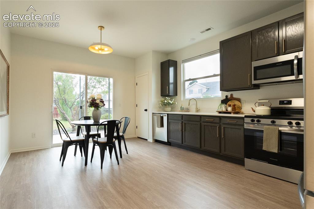 Image 8 of 26: Modern kitchen featuring dark cabinetry, stainless steel appliances, and wo