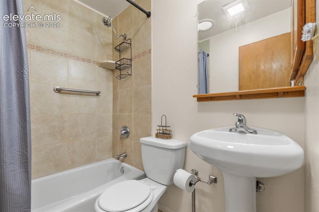Image 16 of 32: Updated main-level bathroom featuring a pedestal sink and tiled tub/shower