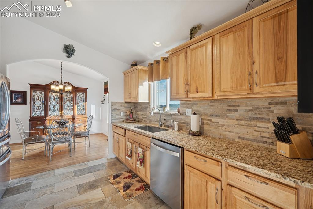 Image 23 of 45: Walk through kitchen features granite countertops, stone backsplash and cus