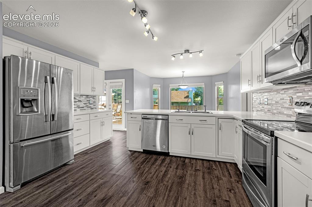 Image 3 of 49: Spacious kitchen featuring wood-finish flooring, white cabinetry, stainless