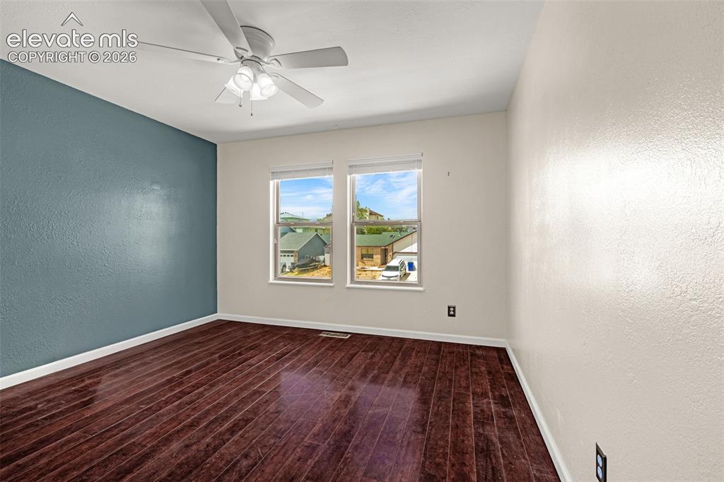 Image 39 of 49: Interior room featuring dark wood-finish flooring, two windows with white t