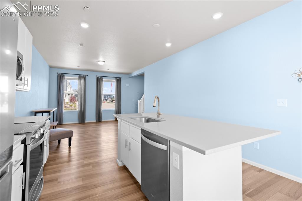 Image 6 of 26: Kitchen with an island with sink, white cabinetry, a sink, light wood-style