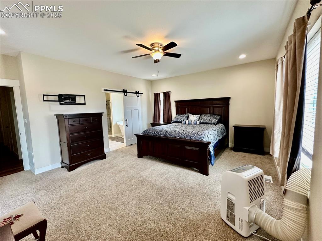 Image 14 of 38: Bedroom featuring a barn door, recessed lighting, light carpet, ensuite bat