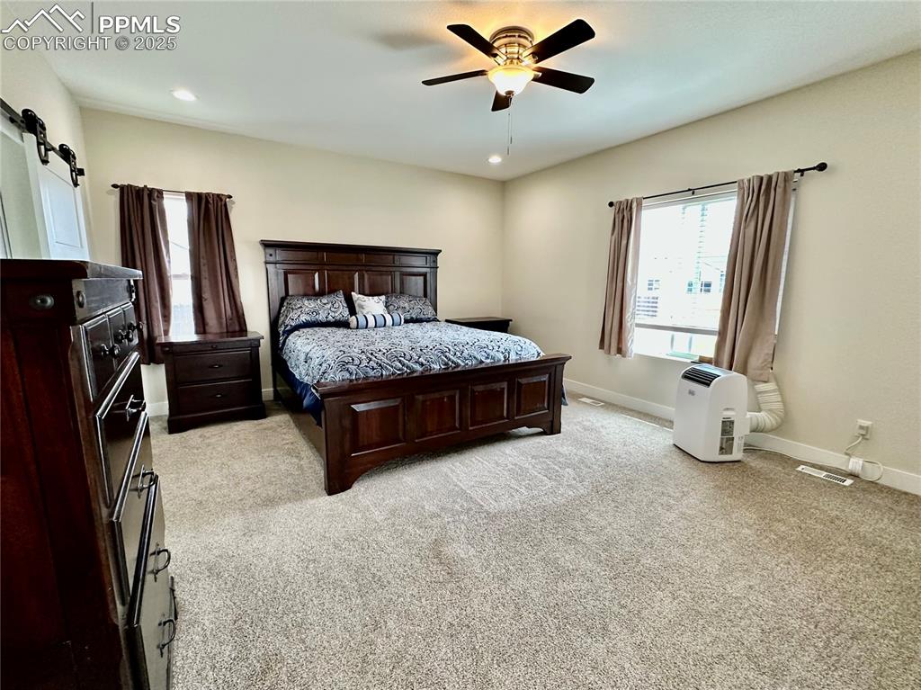 Image 16 of 38: Bedroom featuring a barn door, light carpet, a ceiling fan, and recessed li