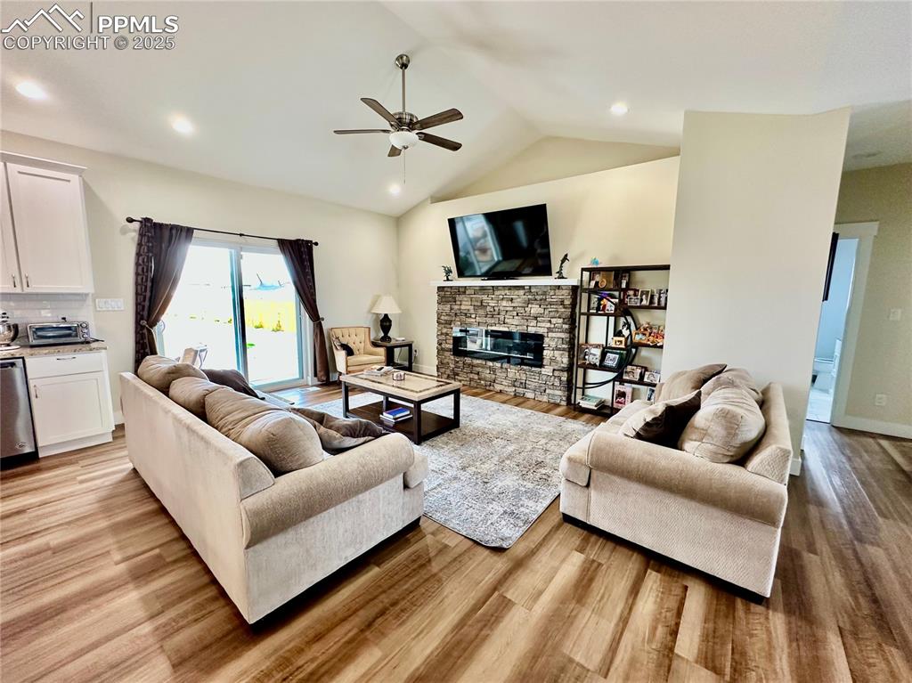 Image 7 of 38: Living room with vaulted ceiling, a stone fireplace, light wood-style floor