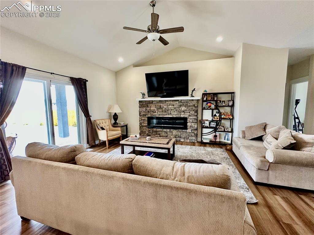 Image 8 of 38: Living room featuring vaulted ceiling, a stone fireplace, wood finished flo