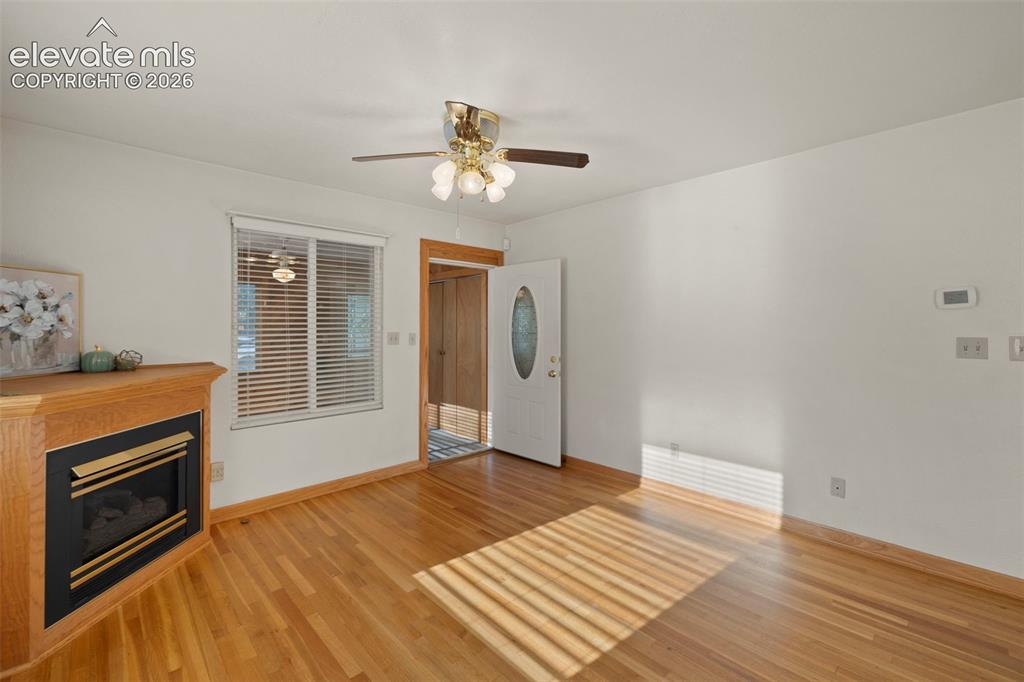 Image 12 of 44: Wood-finish flooring, corner fireplace with a wood mantle, ceiling fan with