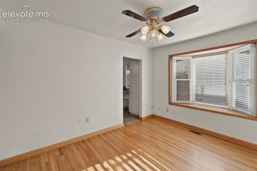 Image 16 of 44: Hardwood flooring, bay window with plantation shutters, ceiling fan with in