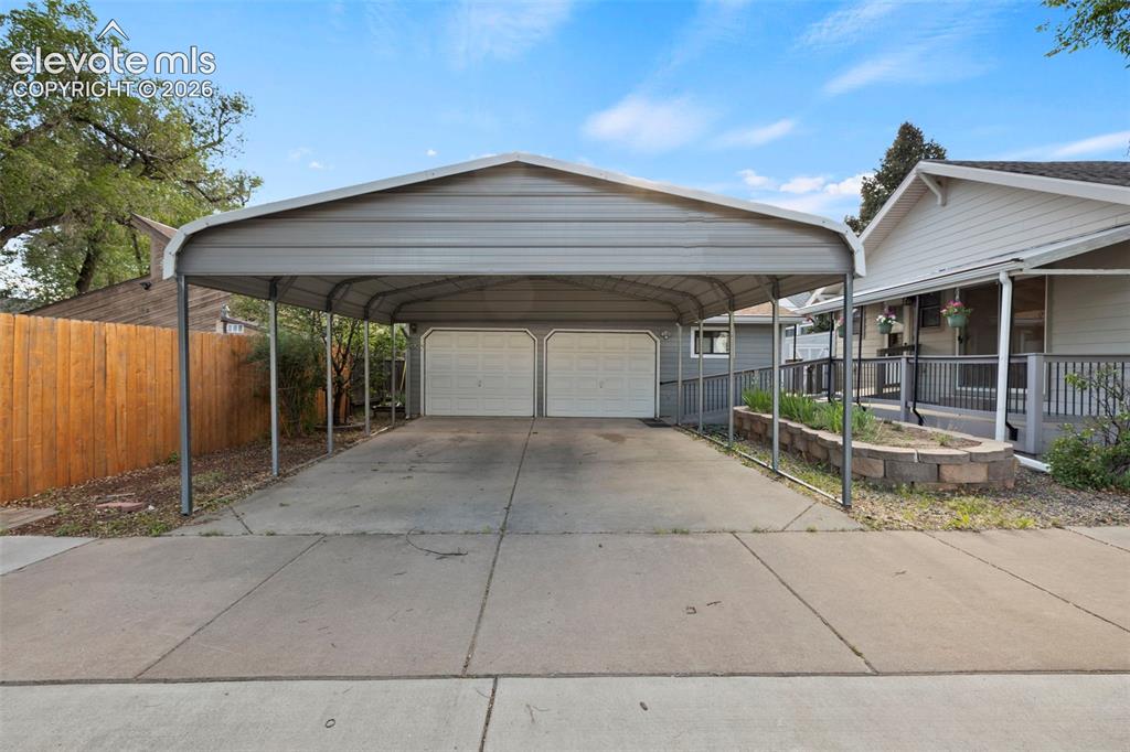 Image 35 of 44: Covered carport with concrete driveway leading to two garage doors