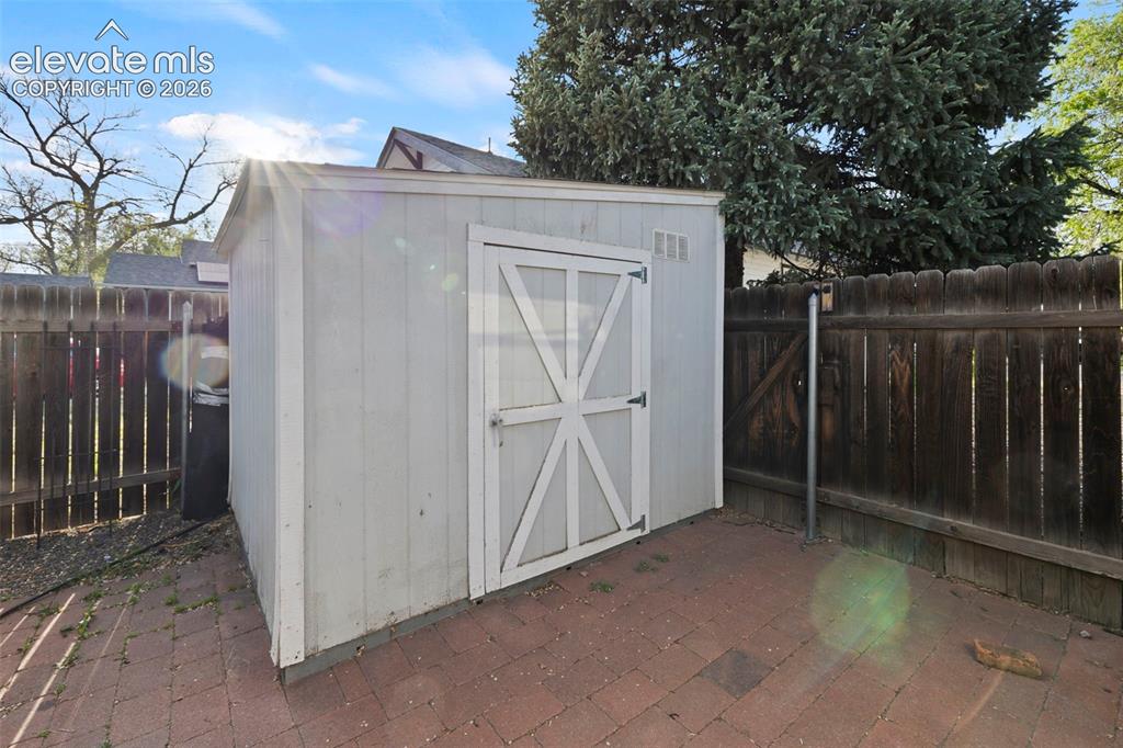 Image 39 of 44: Storage shed with a barn-style door, set on a brick paver patio, featuring 