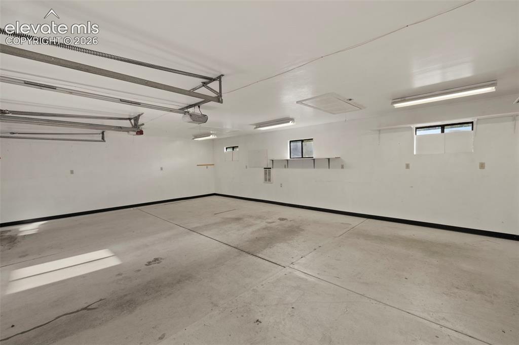 Image 42 of 44: Spacious garage with concrete flooring, multiple windows, built-in shelving