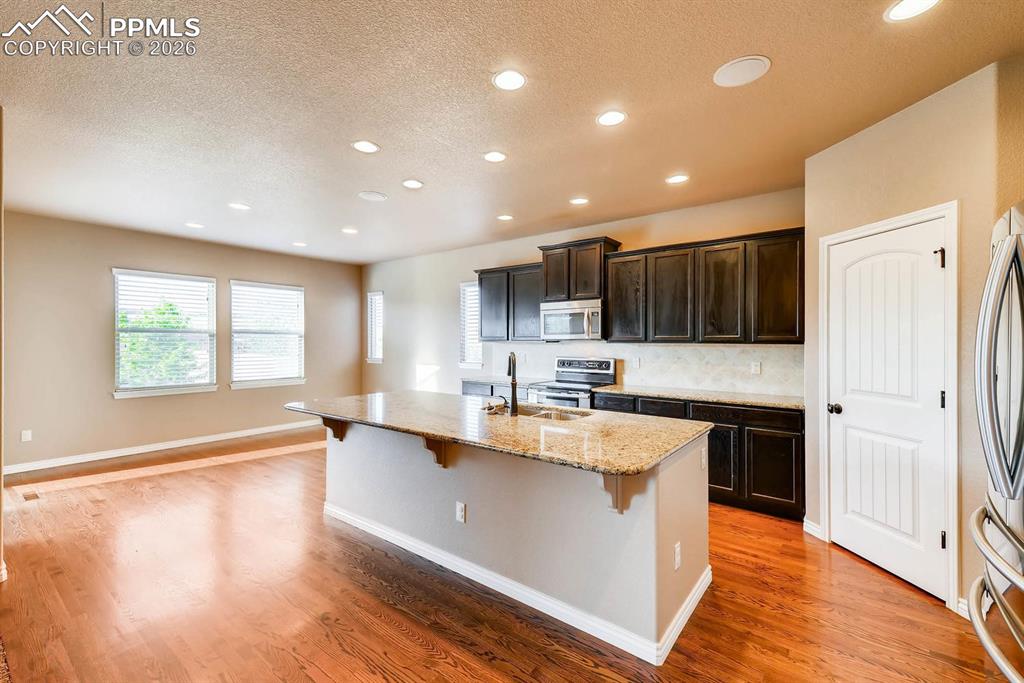 Image 11 of 28: Kitchen with a textured ceiling, a breakfast bar, light stone countertops,
