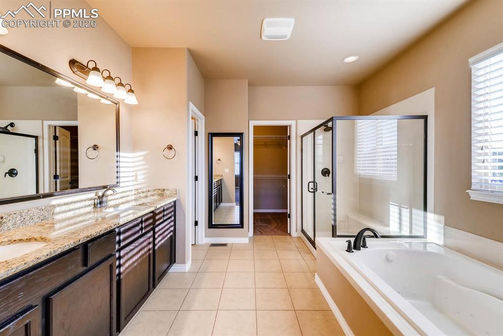 Image 15 of 28: Full bathroom with a walk in closet, double vanity, a shower stall, a garde