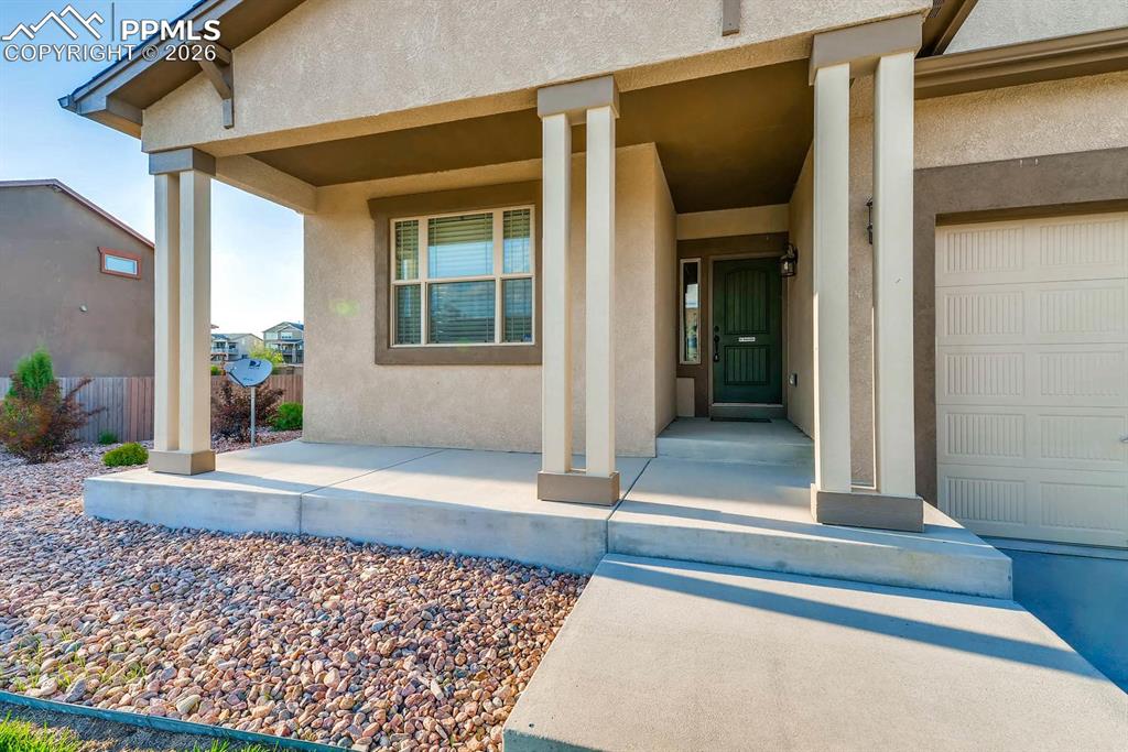 Image 3 of 28: View of exterior entry with stucco siding, covered porch, and a garage