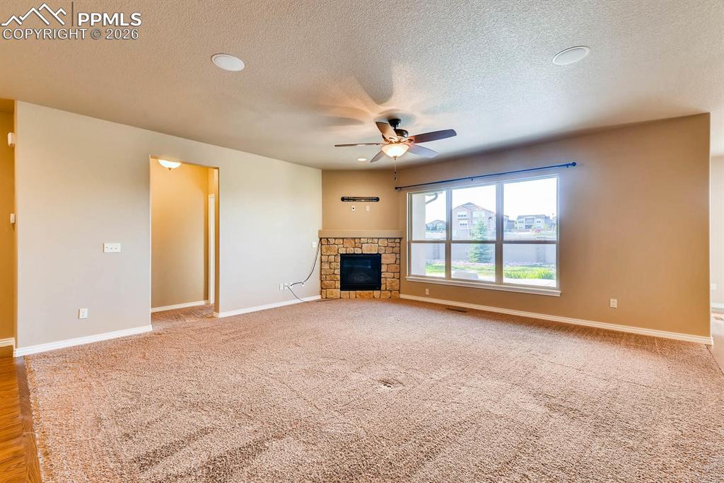 Image 6 of 28: Unfurnished living room with ceiling fan, light carpet, a fireplace, and a