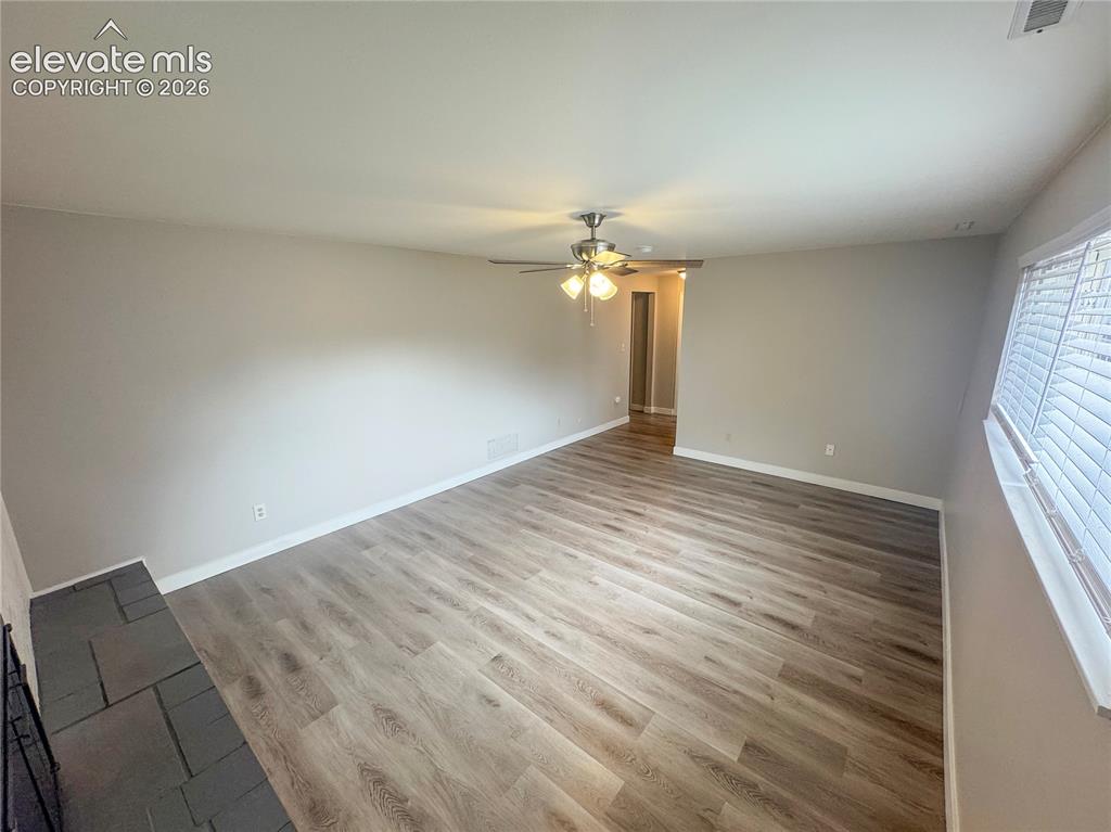 Image 28 of 42: Wood-finish flooring, stone hearth, and central ceiling fan with integrated