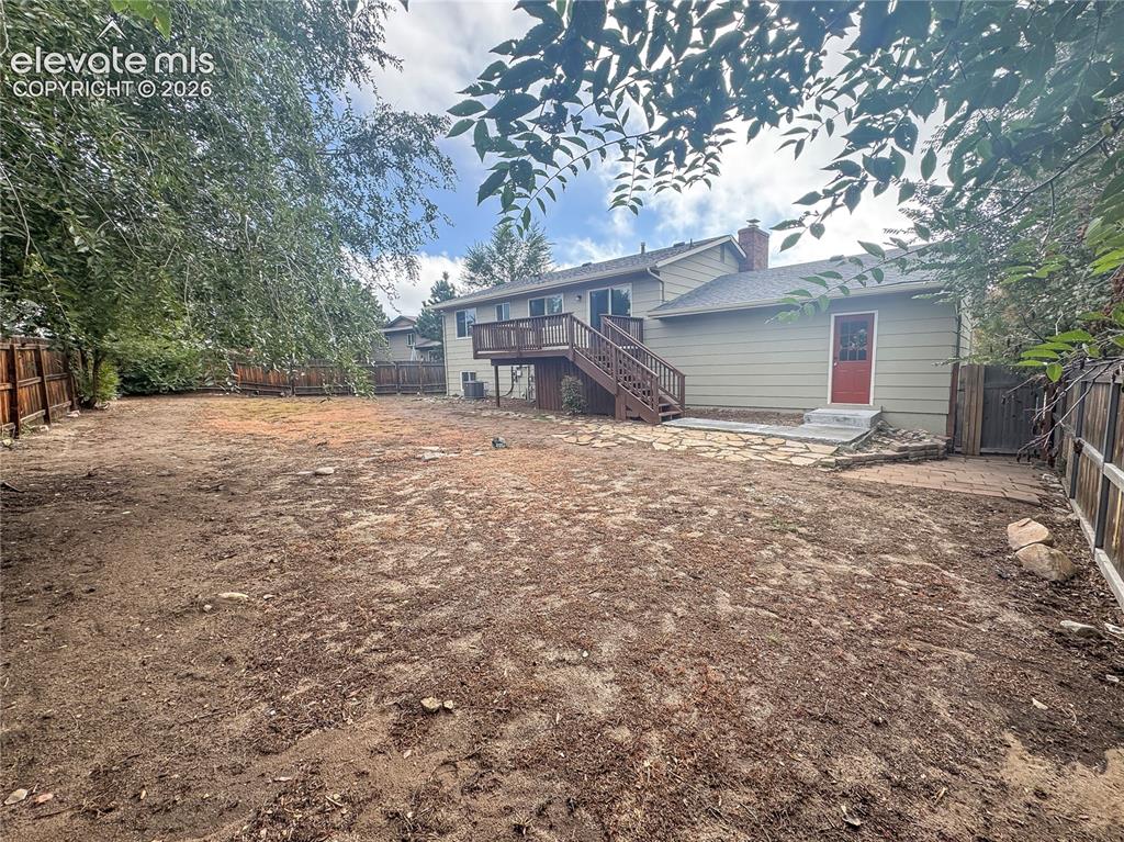 Image 36 of 42: Backyard featuring a raised wooden deck, a stone patio, mature trees, and p