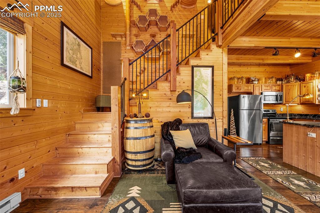 Image 15 of 45: Living room featuring wooden walls, stairs, dark wood-style flooring, a bas