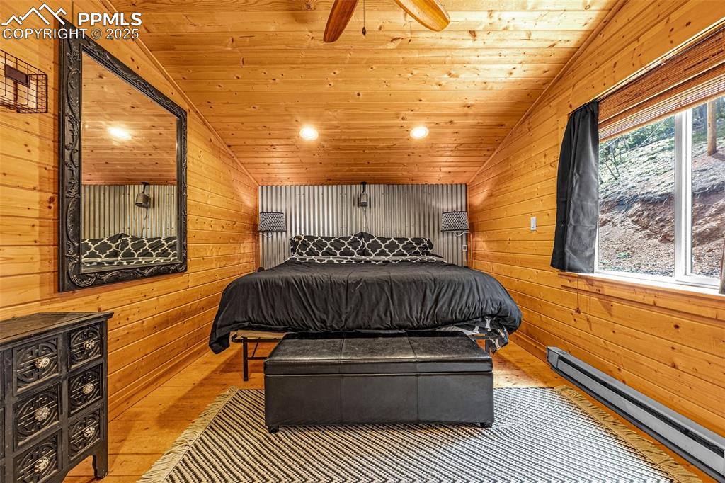 Image 19 of 45: Bedroom with a baseboard radiator, lofted ceiling, wood walls, wood finishe