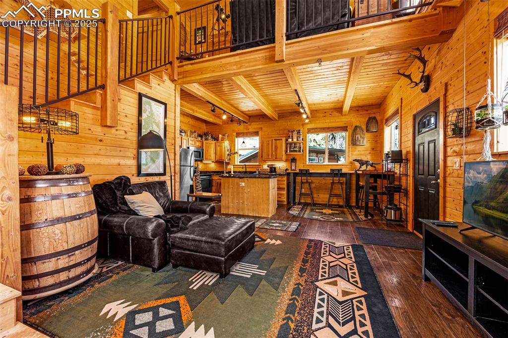 Image 7 of 45: Living room with wood walls, dark wood-style floors, beam ceiling, and wood