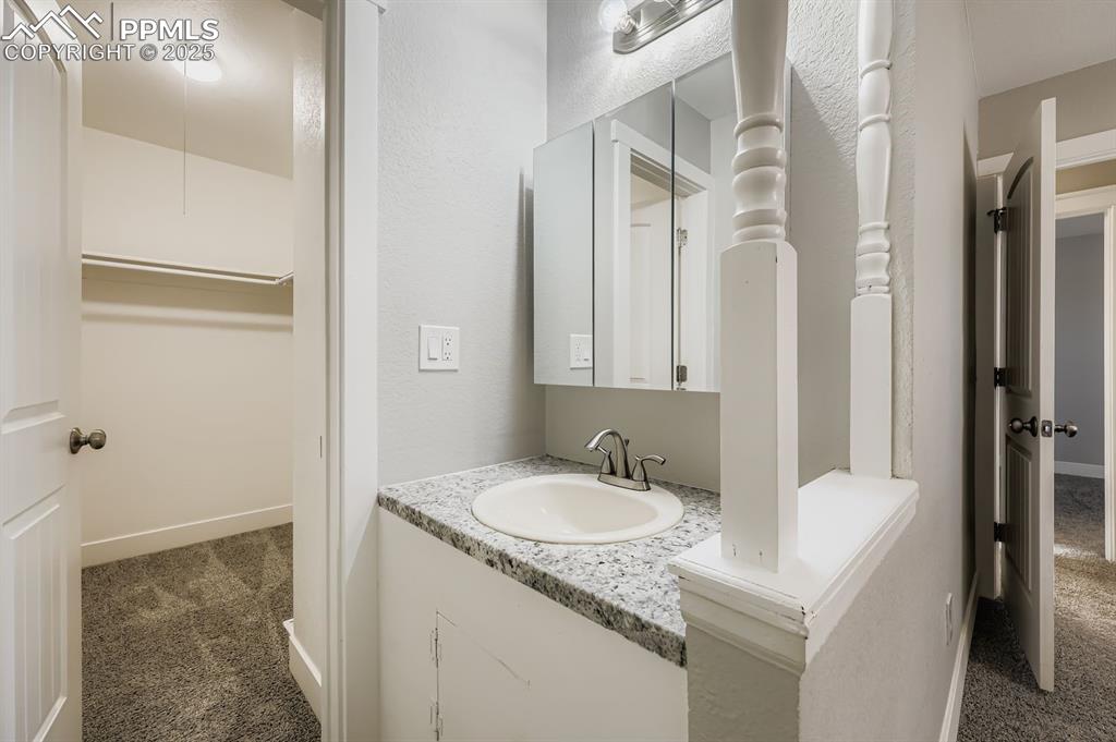 Image 12 of 28: Bathroom with dark carpet, a walk in closet, vanity, and a textured wall