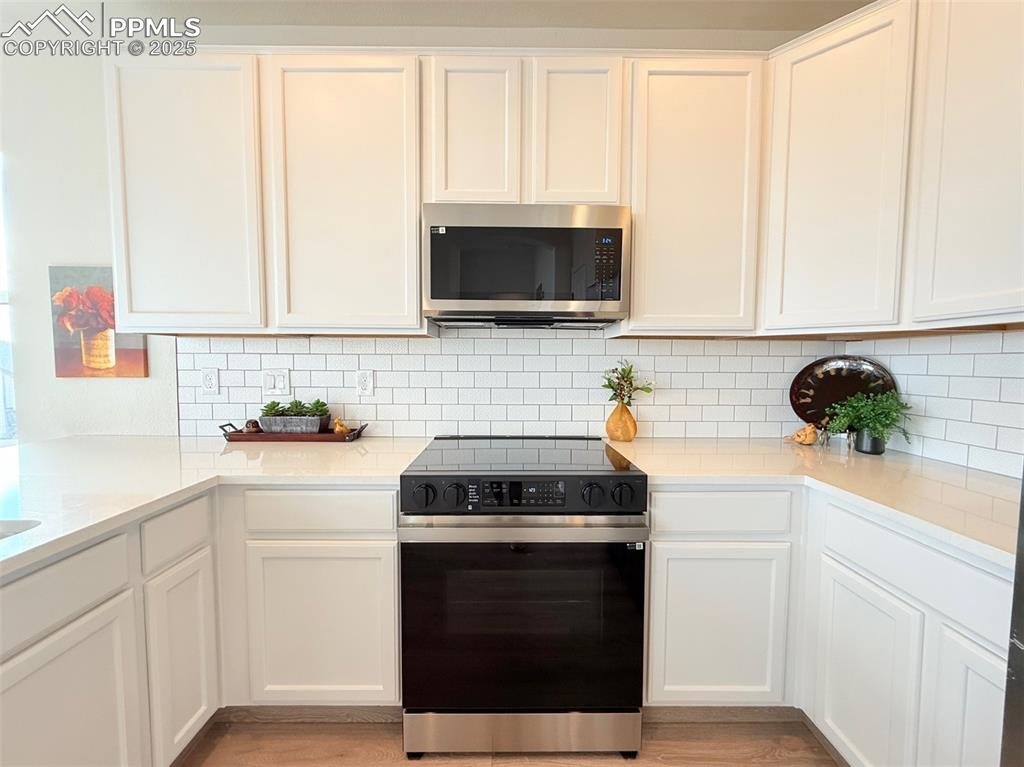 Image 15 of 49: Kitchen with range with electric stovetop, stainless steel microwave, white