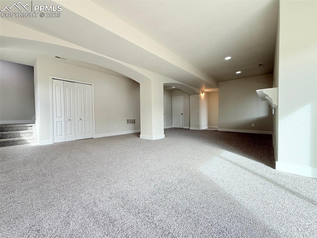 Image 31 of 49: Unfurnished living room featuring arched walkways, carpet, stairway, and re