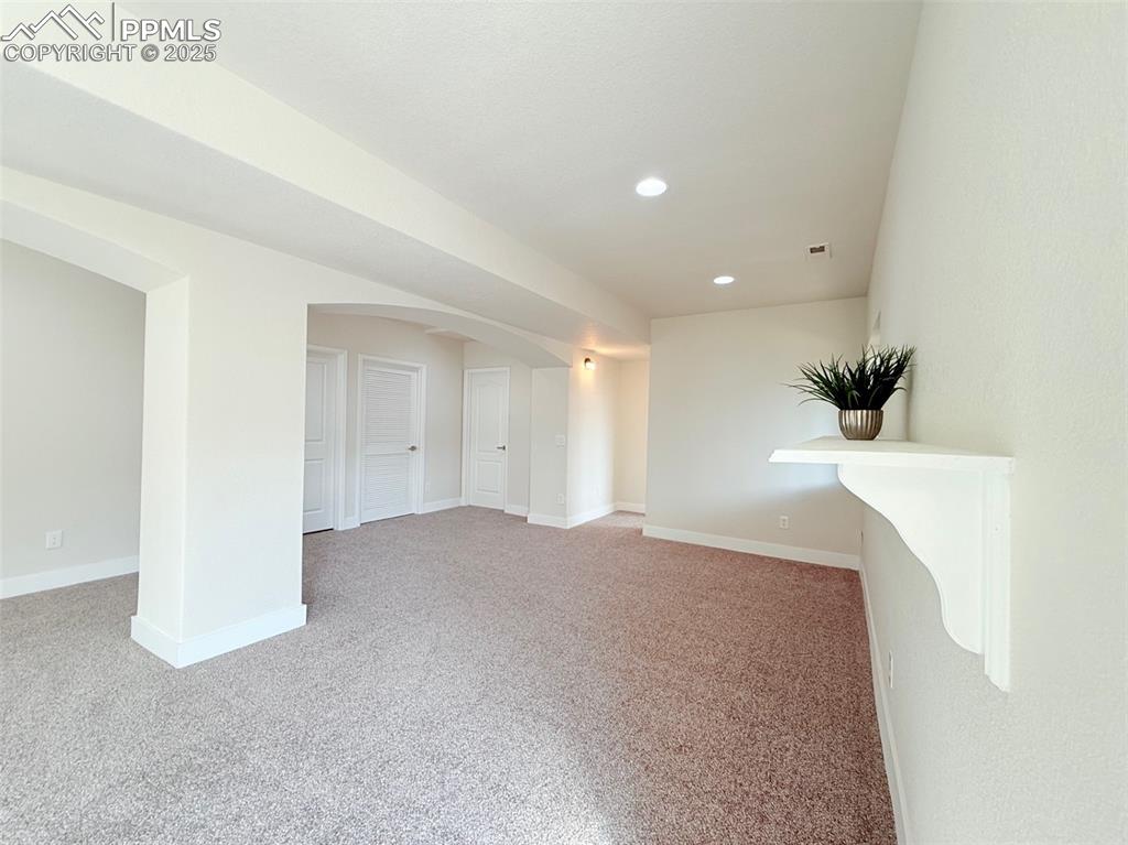 Image 34 of 49: Empty room with arched walkways, light carpet, and recessed lighting