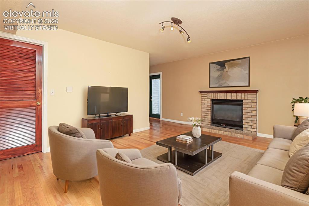 Image 10 of 32: Living area featuring wood-finish flooring, a brick-surround fireplace with