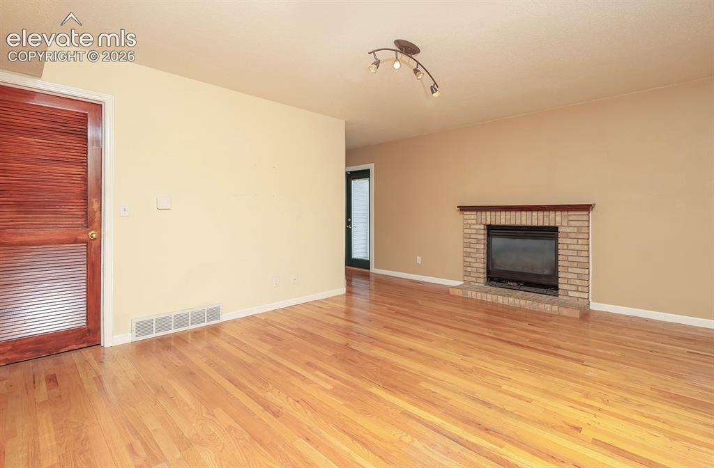 Image 28 of 32: Light wood-finish flooring with a brick fireplace featuring a dark wood man