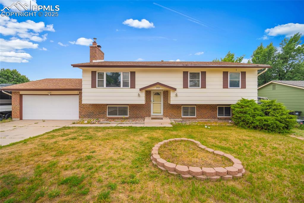 Caption: Raised ranch featuring a garage, a chimney, brick siding, and a front yard
