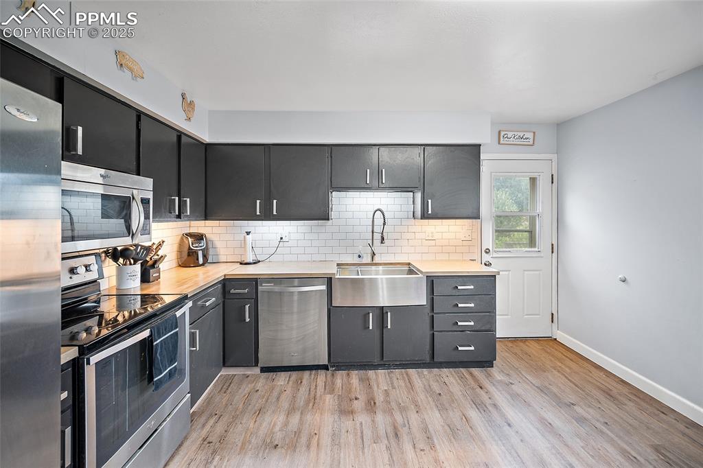 Image 27 of 49: Kitchen with stainless steel appliances, tasteful backsplash, light wood fi
