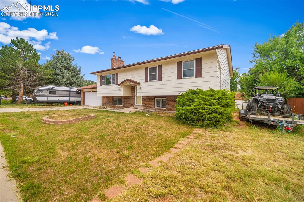 Image 3 of 49: Bi-level home with brick siding, a chimney, driveway, and a front yard