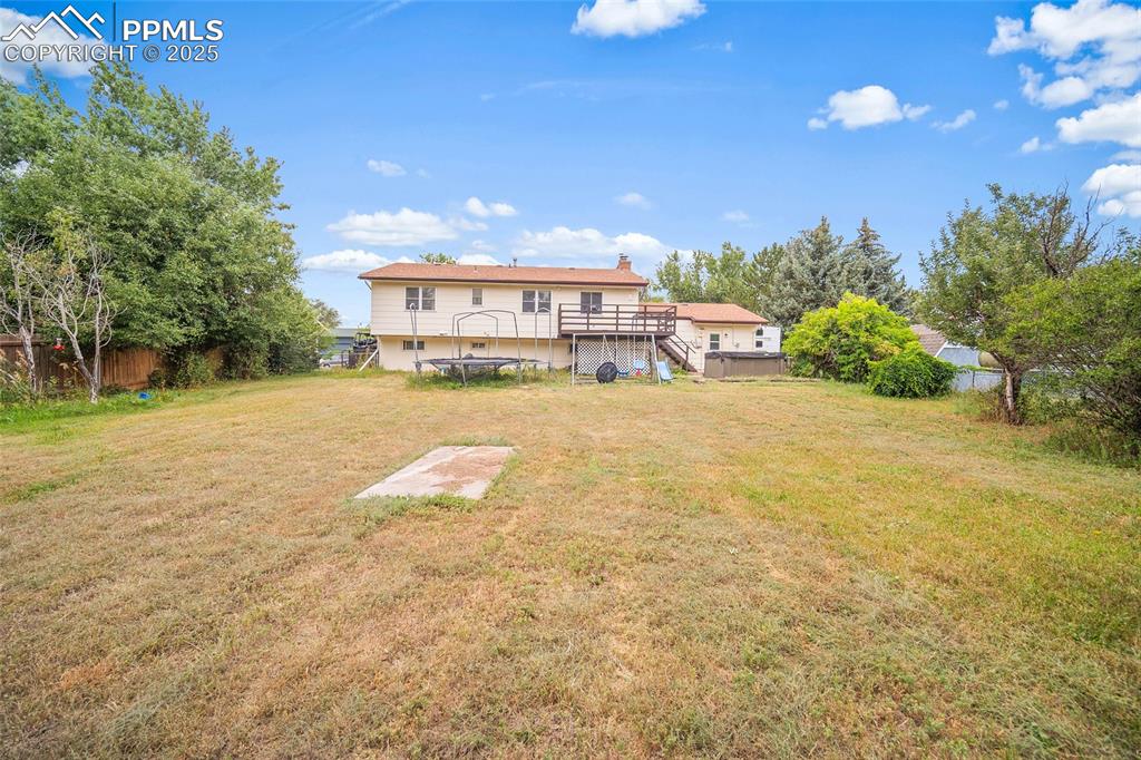 Image 34 of 49: Rear view of house featuring a wooden deck, stairs, a chimney, and a trampo