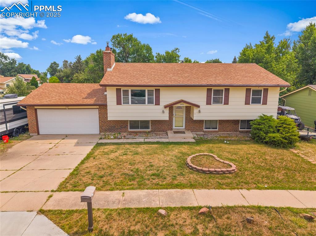 Image 37 of 49: Bi-level home with a front yard, a garage, a chimney, brick siding, and dri