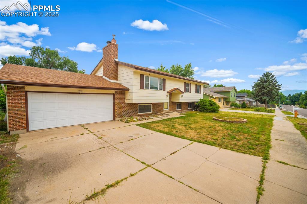 Image 4 of 49: Raised ranch with brick siding, an attached garage, driveway, a front yard,