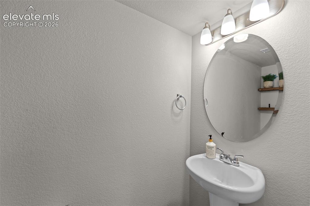 Image 11 of 32: Pedestal sink with chrome faucet, oval mirror, and wall-mounted light fixtu