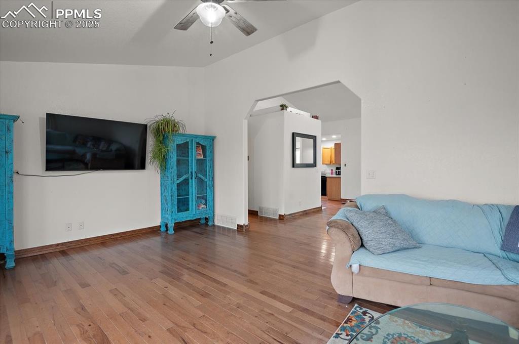 Image 15 of 38: Living area with a ceiling fan, wood finished floors, baseboards, and arche